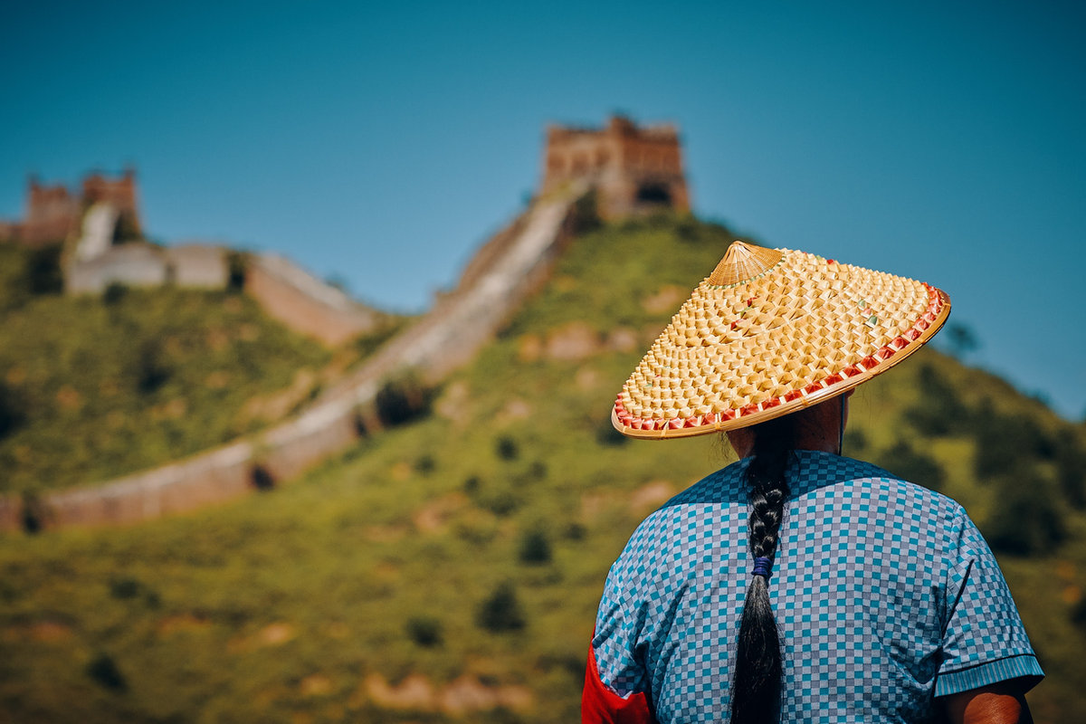 A traveler in a woven hat looking out over the Great Wall of China
